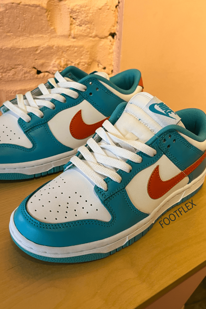 Side view of Nike Low Dunk Retro sneakers in white with turquoise and red accents, featuring a sleek design and signature Nike swoosh.